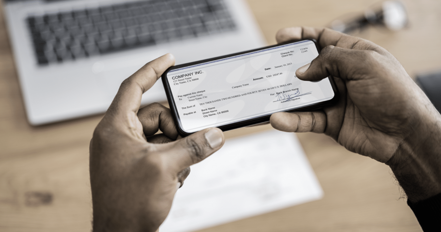 Person scanning a check using a smartphone with a laptop nearby.