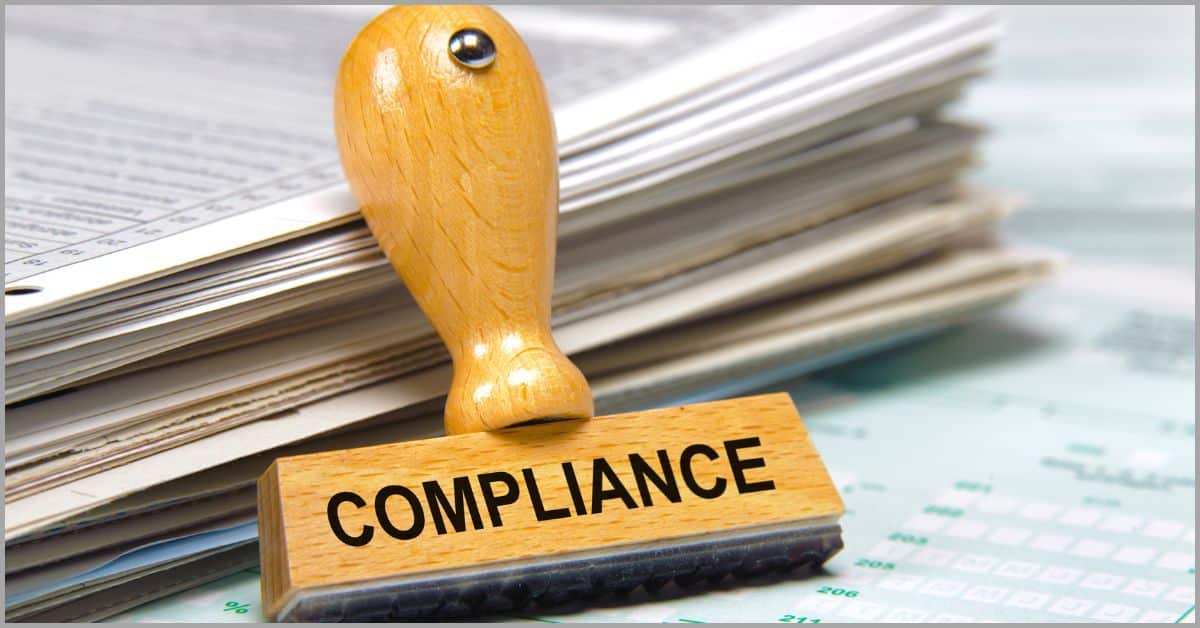 Rubber stamp labeled 'Compliance' placed on stacked documents.